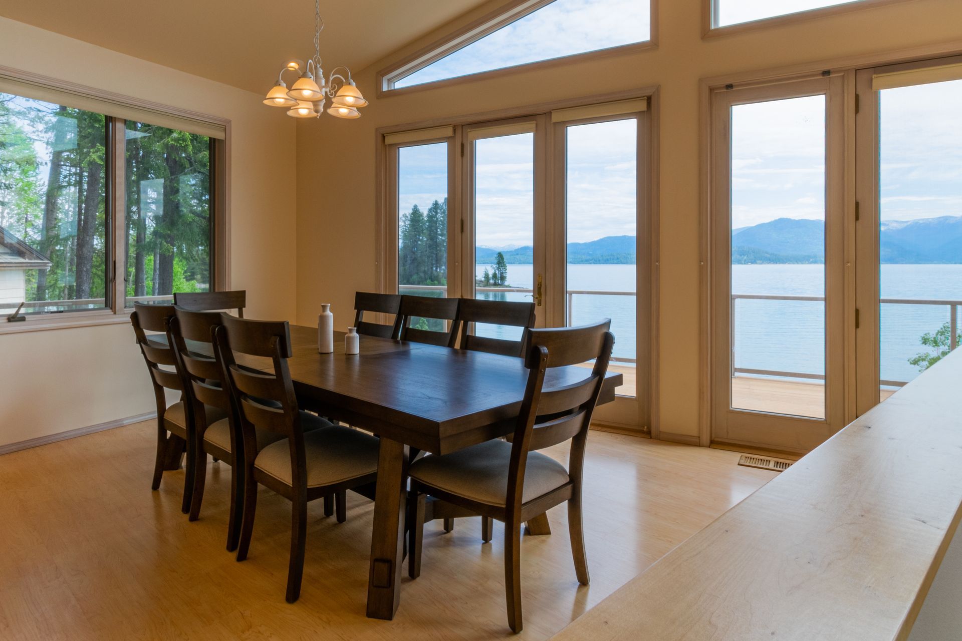Dining room with large table and chairs, overlooking a lake through floor-to-ceiling windows.