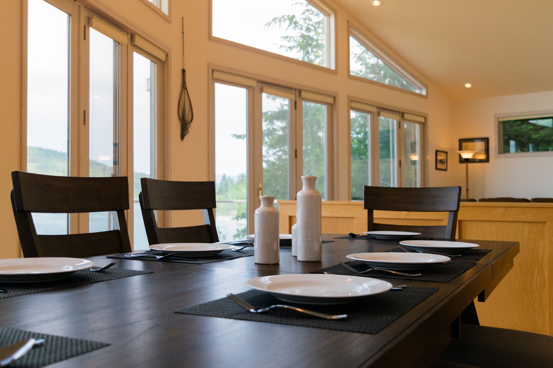 Dining room with dark wooden table set for a meal; large windows offer an outdoor view.