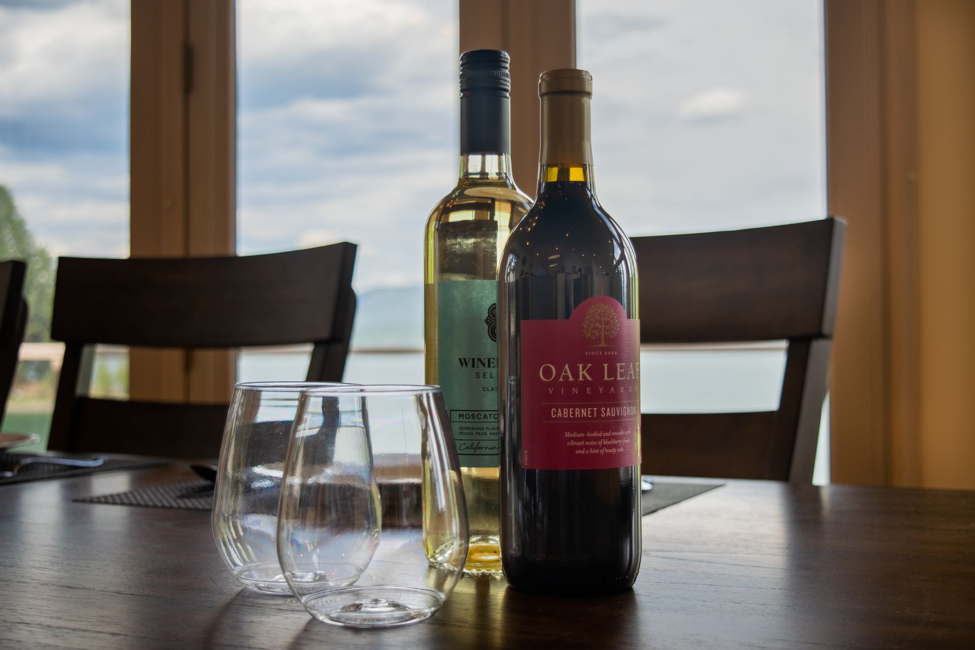 Two wine bottles, one white and one red, on a wooden table with two empty glasses.