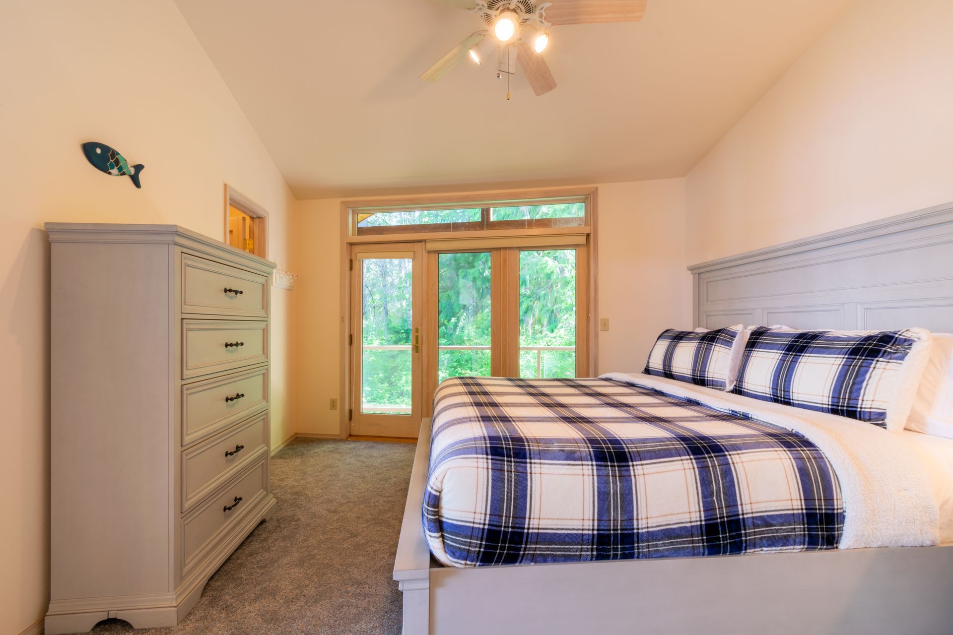 Bedroom with gray dresser, blue and white plaid bedding, and French doors opening to a green outdoor view.