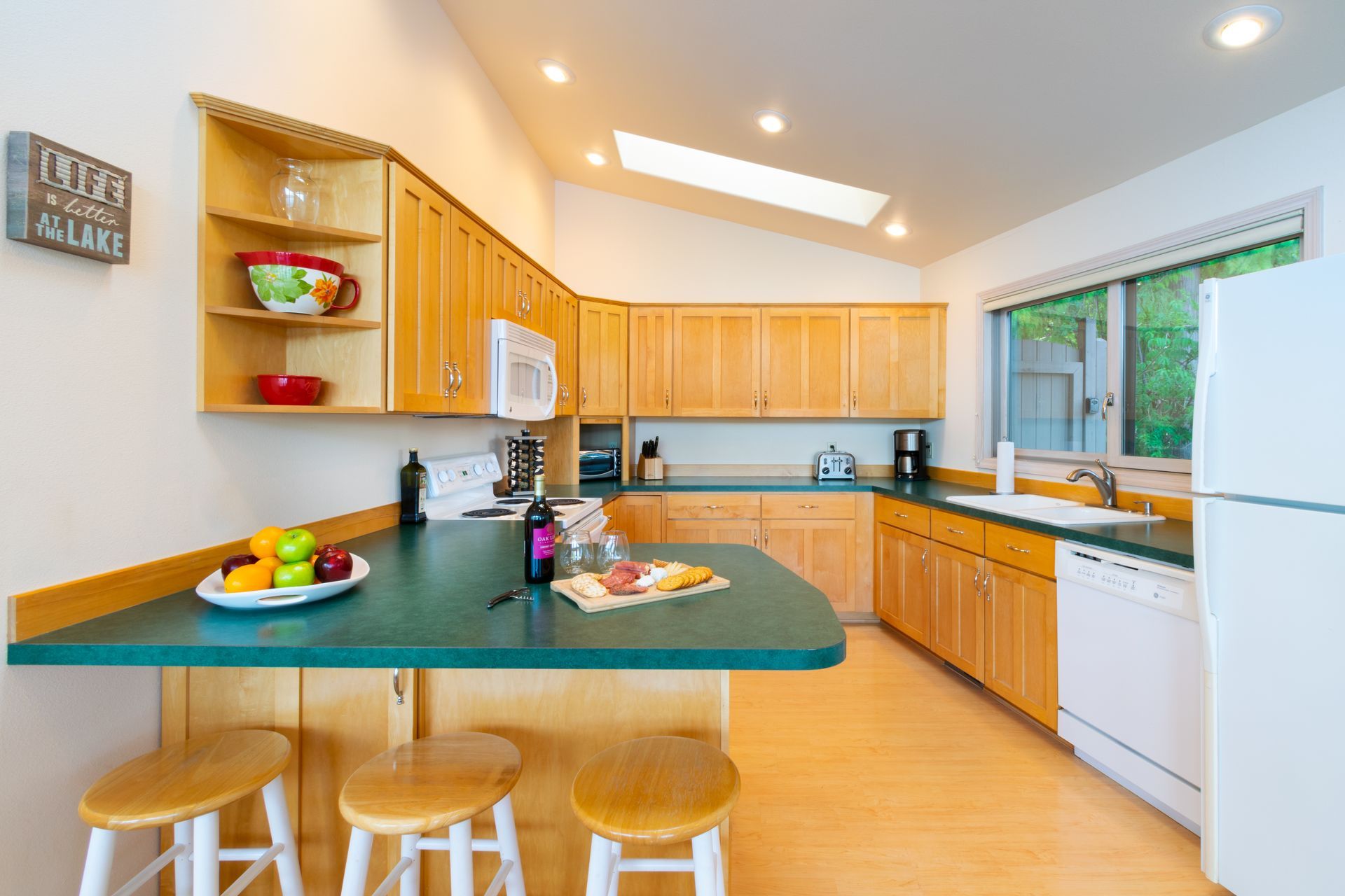 A kitchen with light wood cabinets, green countertops, and a breakfast bar with three stools.