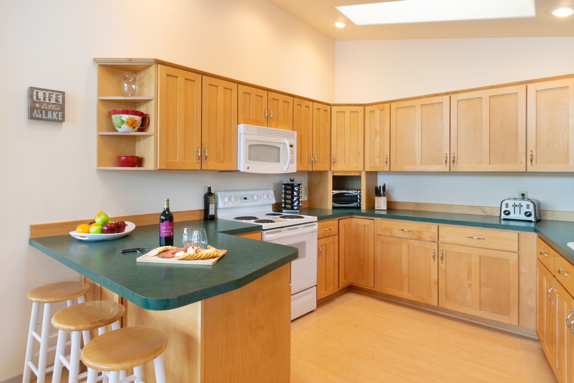 Kitchen with light wood cabinets, green countertops, and a breakfast bar with stools.