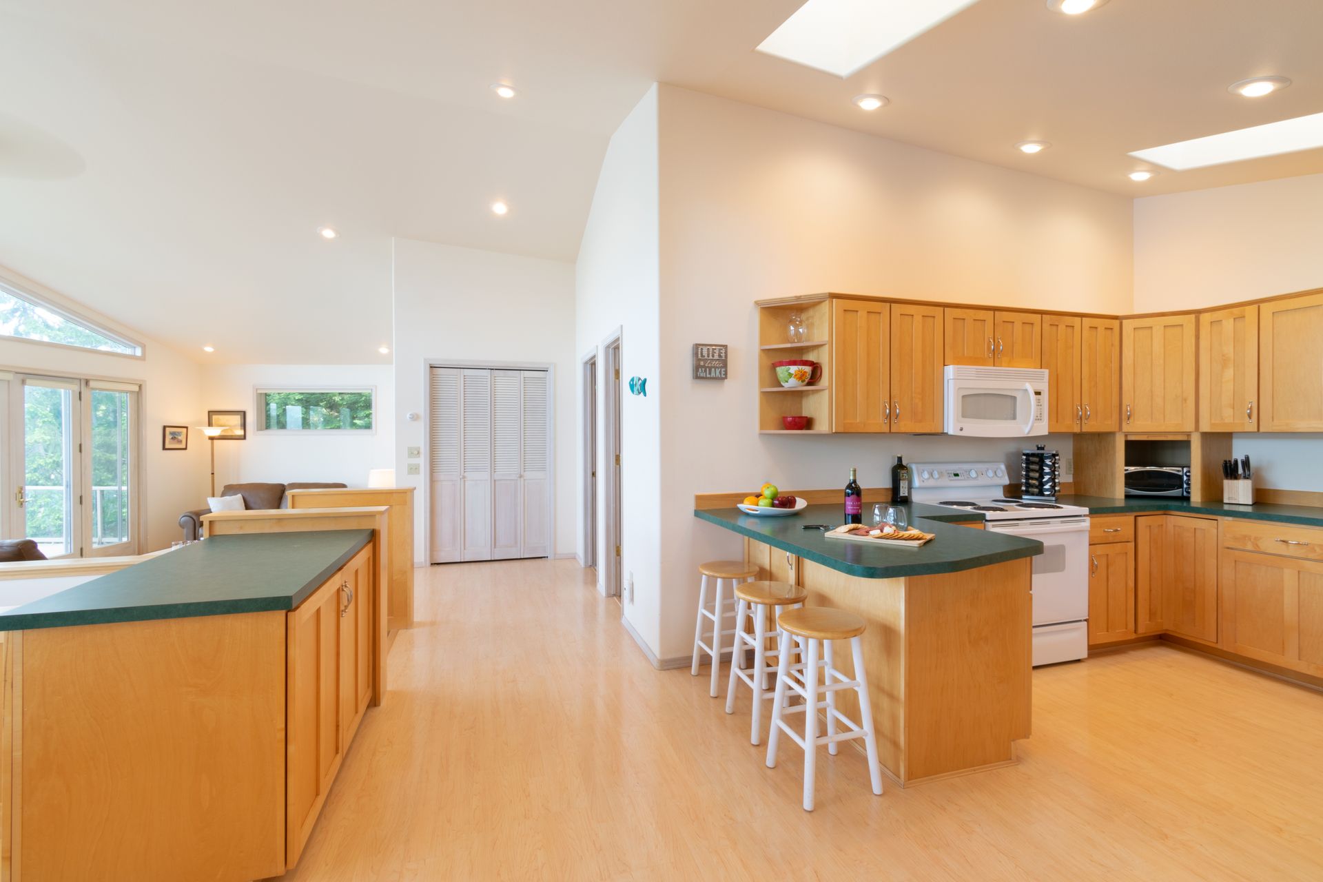 Spacious kitchen with blonde wood cabinets, green countertops, and a breakfast bar with stools.