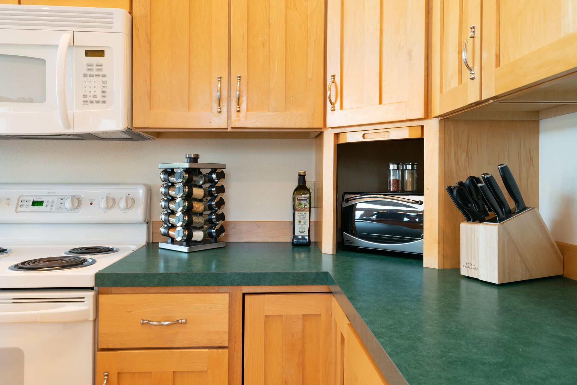 Kitchen corner with light wood cabinets, green countertop, and appliances.