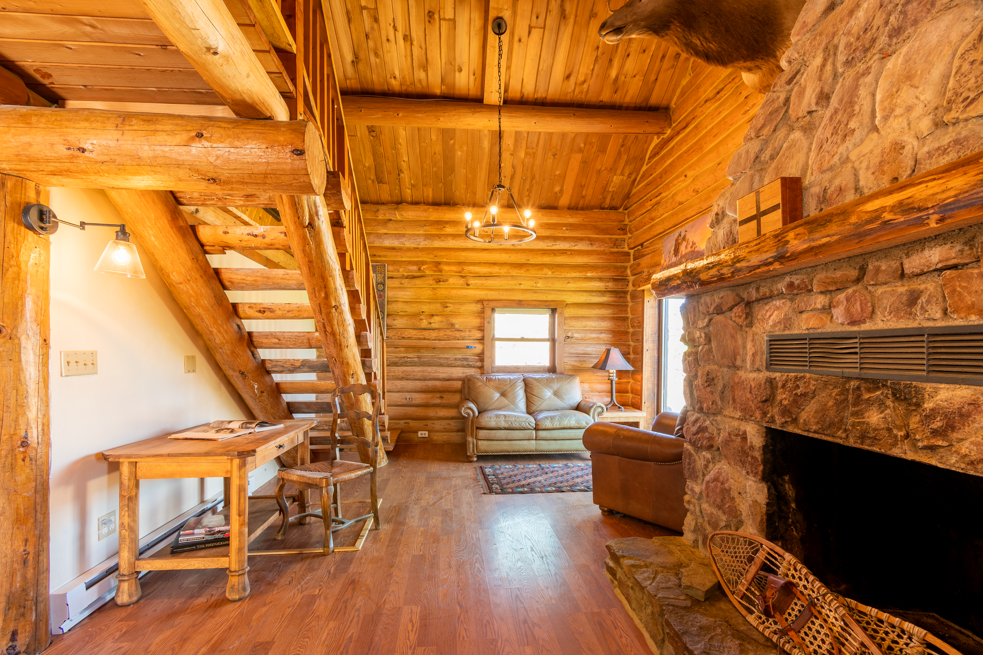 Cozy cabin interior with a stone fireplace, wooden beams, and a loft area with a ladder, creating a rustic ambiance.