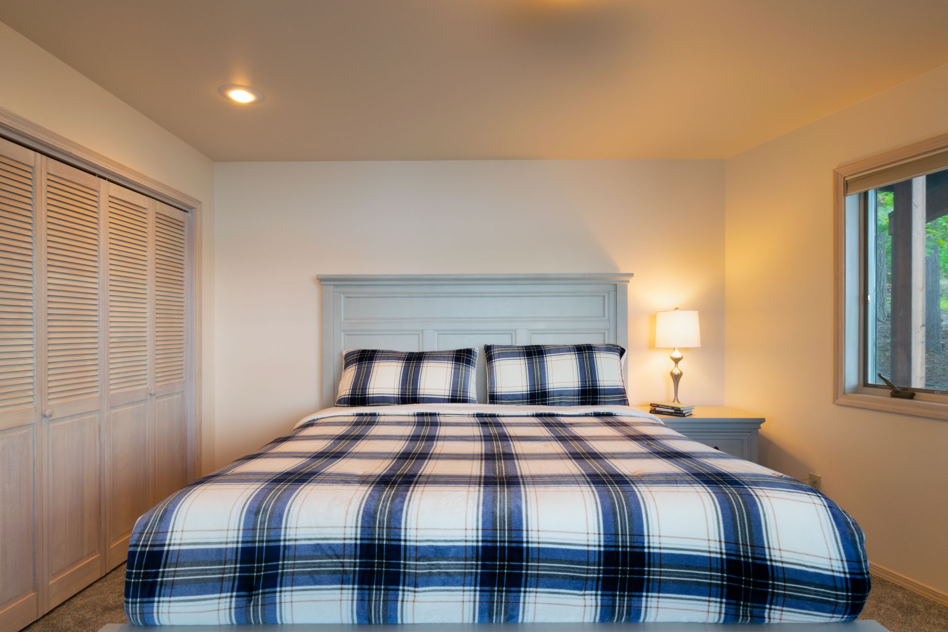 A bedroom with a bed covered in blue and white plaid bedding. A closet is on the left and a window on the right.