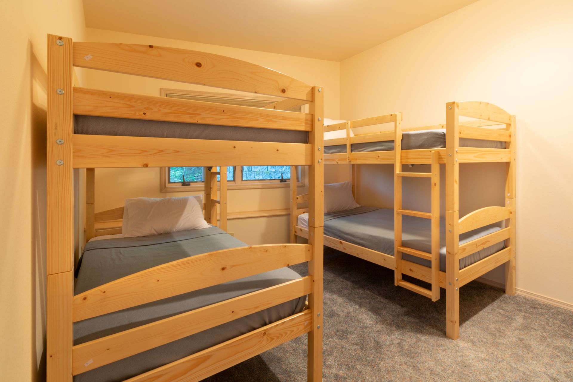 Three wooden bunk beds in a bedroom with grey carpet and tan walls. Two beds are fully made.