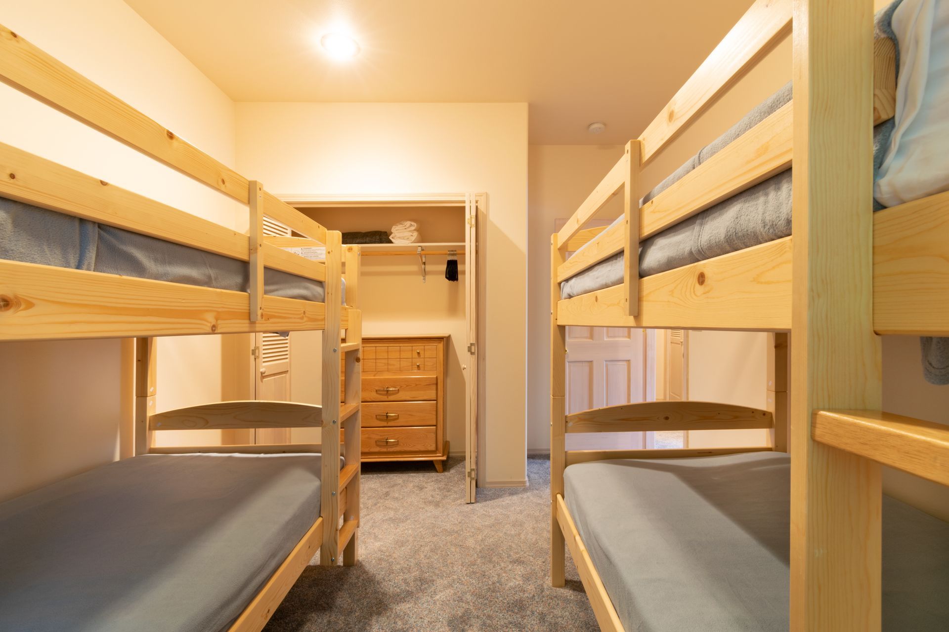 Bedroom with two sets of wooden bunk beds and a closet. The beds have gray mattresses, and the room has gray carpet.