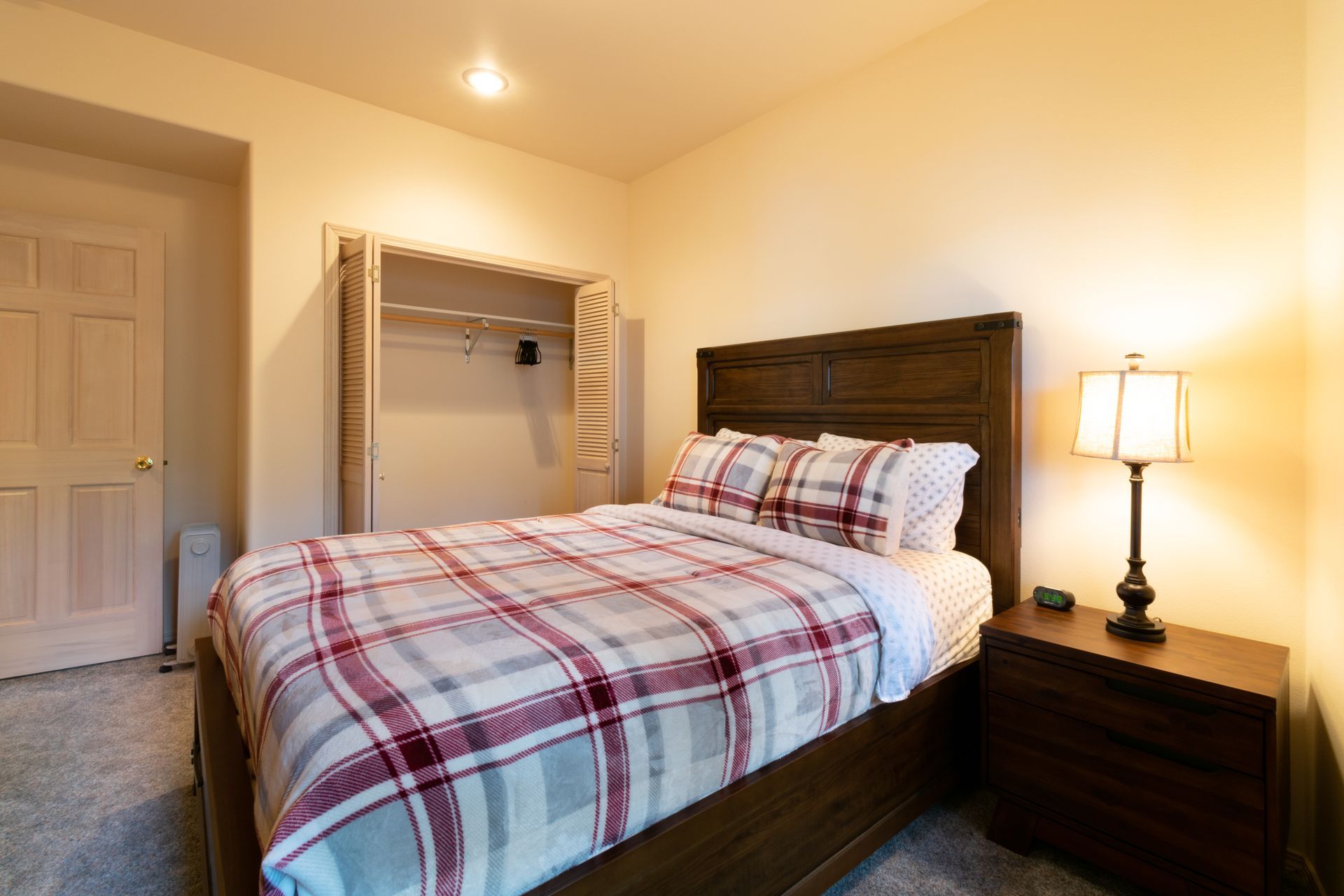 Bedroom with a plaid bedspread, nightstand with lamp, and a closet with open doors.