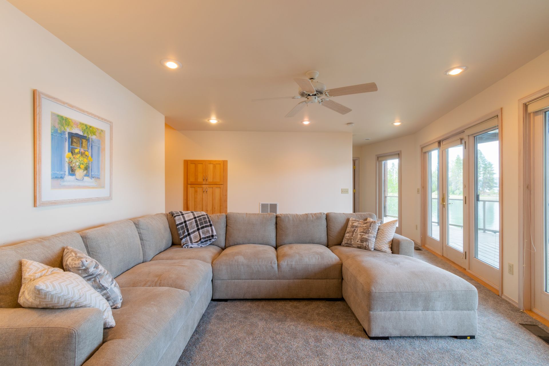 A living room with a large gray sectional sofa, artwork, light walls, and glass doors leading outside.