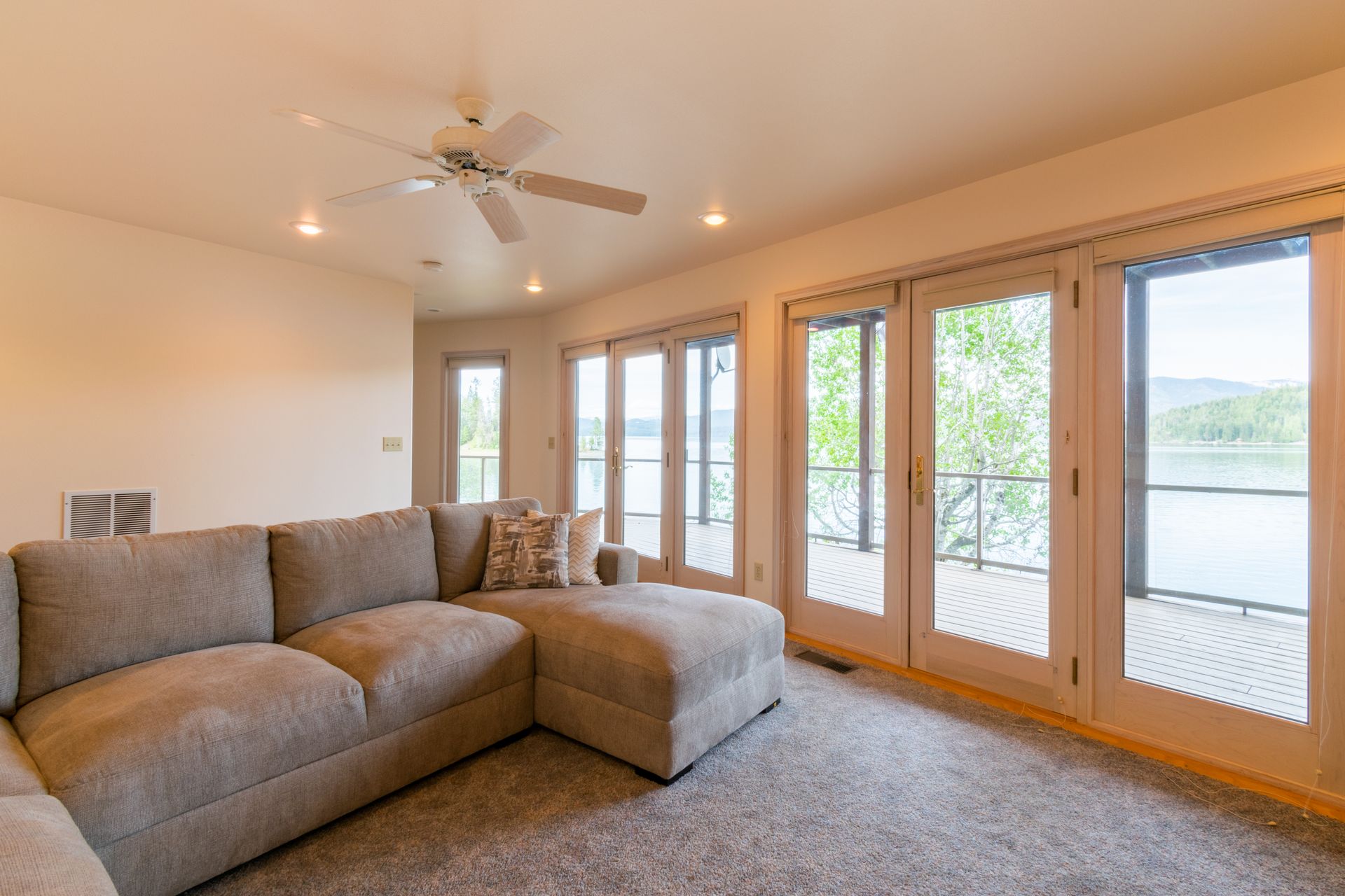 A living room with a gray sectional sofa and large glass doors leading to a deck with a water view.