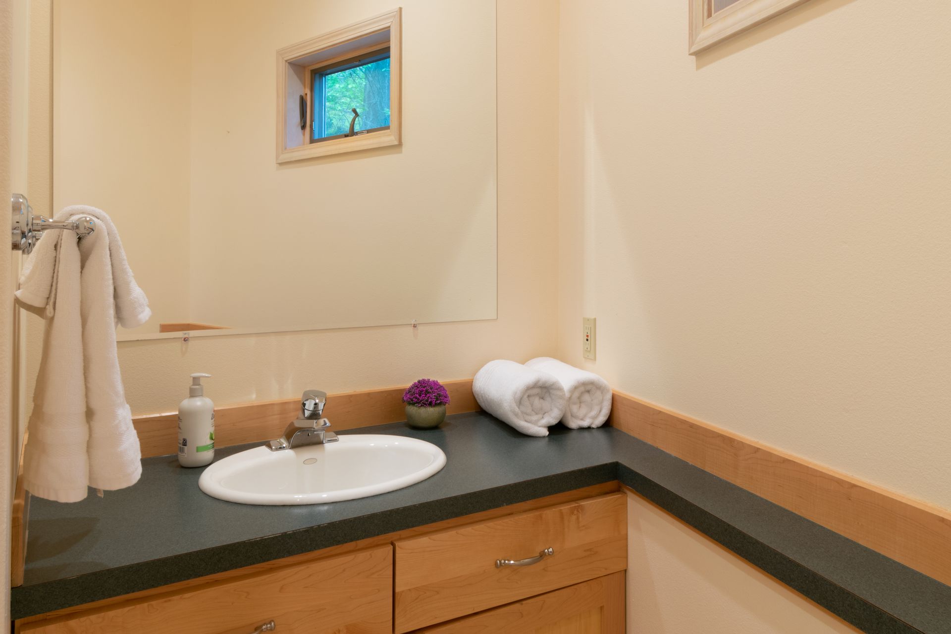 A small bathroom with a sink, mirror, and towels. There is a small window and light-colored walls.