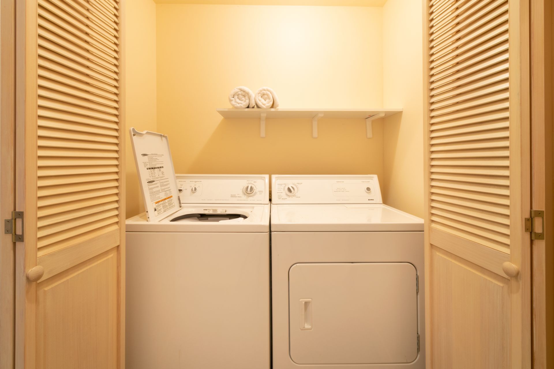 A small laundry room with a washing machine and dryer. The machines are white, set between two shuttered doors.