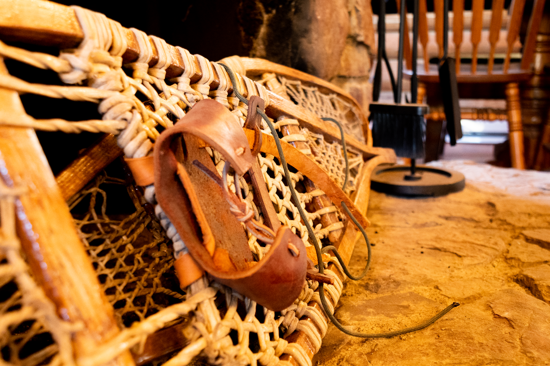 Close-up of a snowshoe with a leather binding resting on a rock surface, suggesting an indoor or rustic setting.