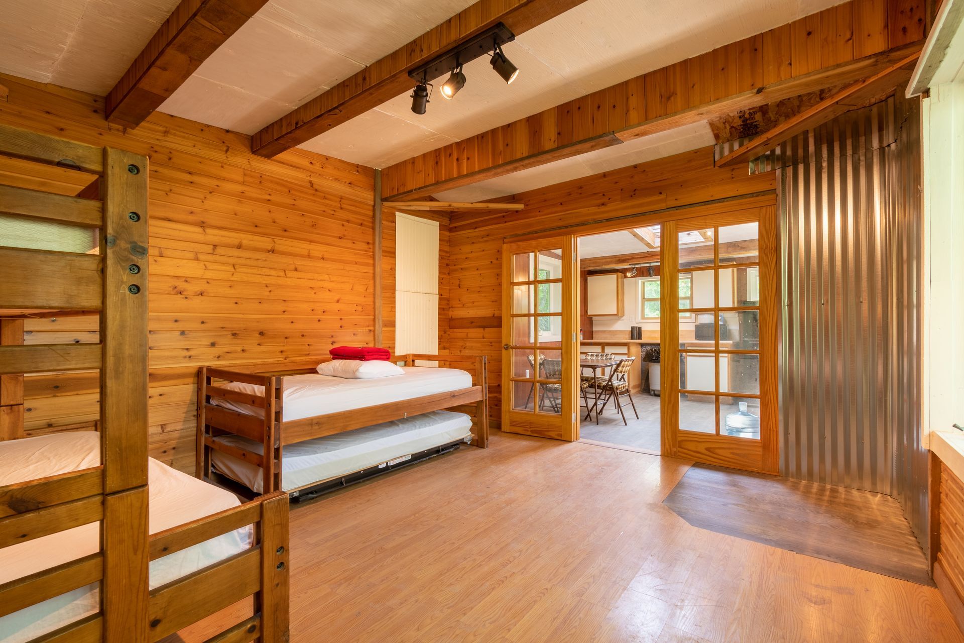 Wooden cabin interior with bunk beds, a pull-out bed, and double doors leading to a kitchen area. The walls are wood-paneled.