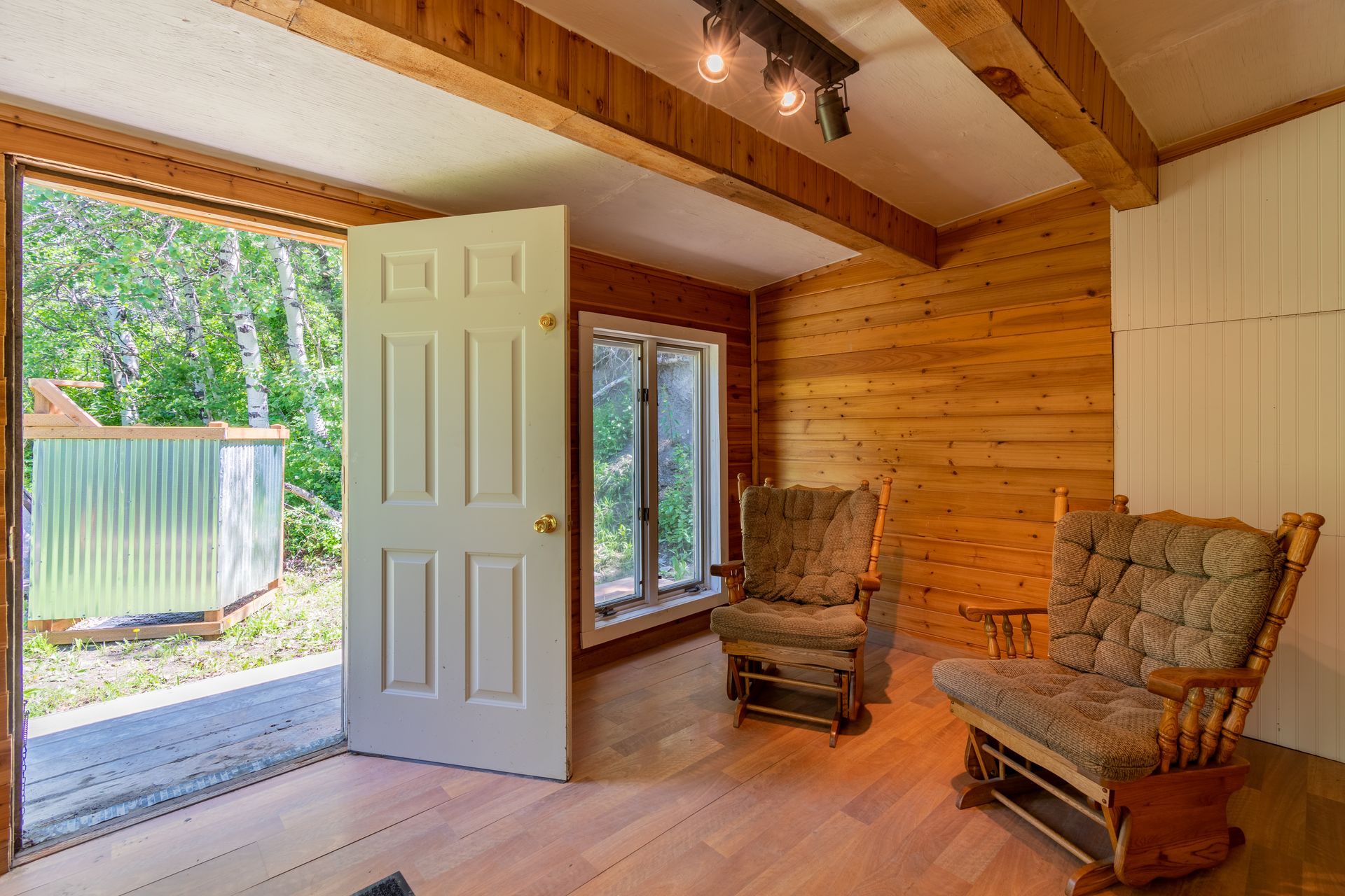 Interior room with wooden walls and floor, two rocking chairs, and an open door leading outside.