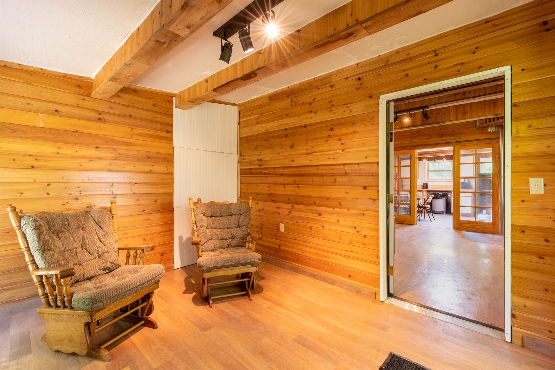 A wood-paneled room with two rocking chairs and an open doorway leading to a workspace with a person.