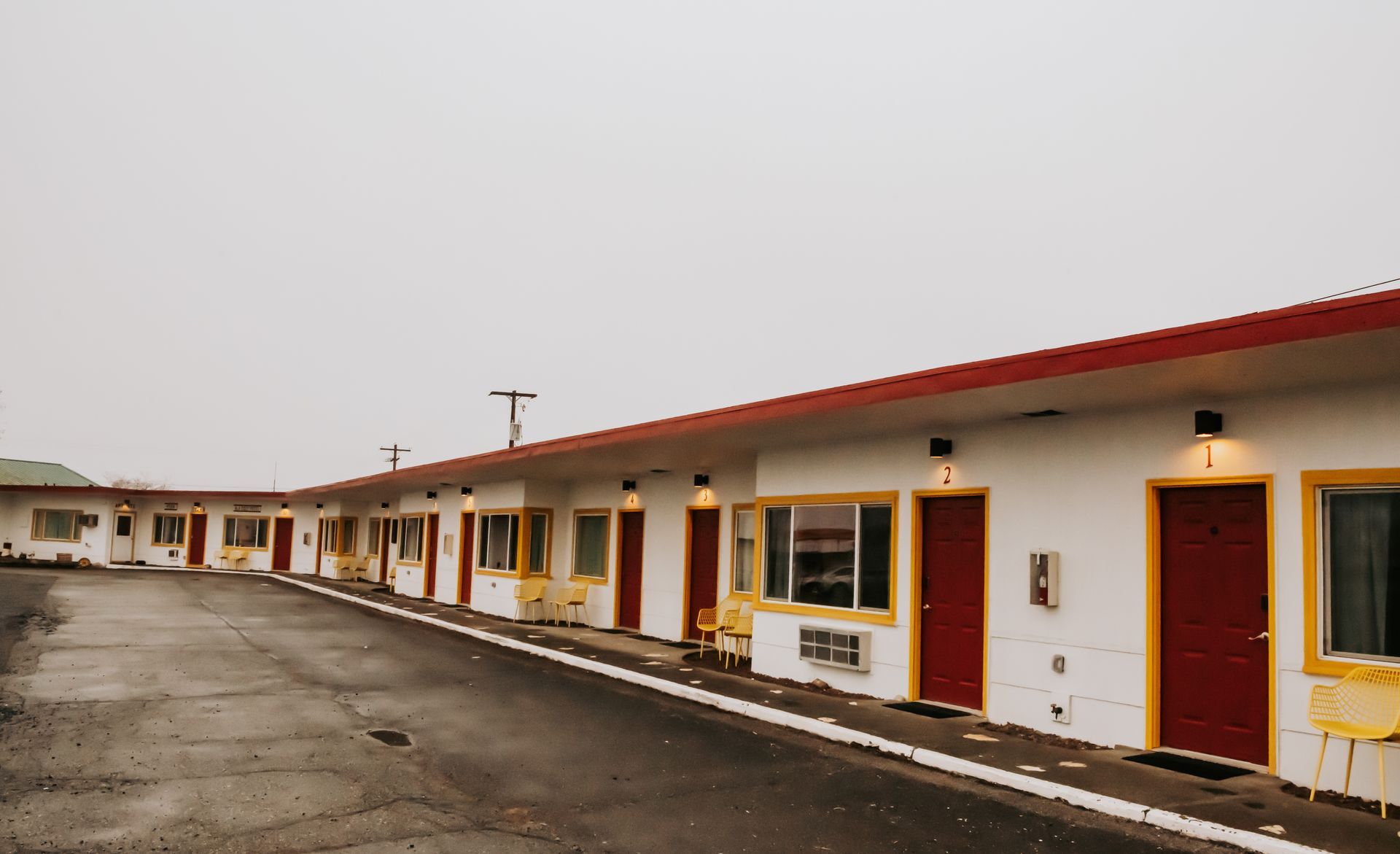 Motel exterior: one-story building with red doors and trim, yellow window frames, white walls, and a flat roof.