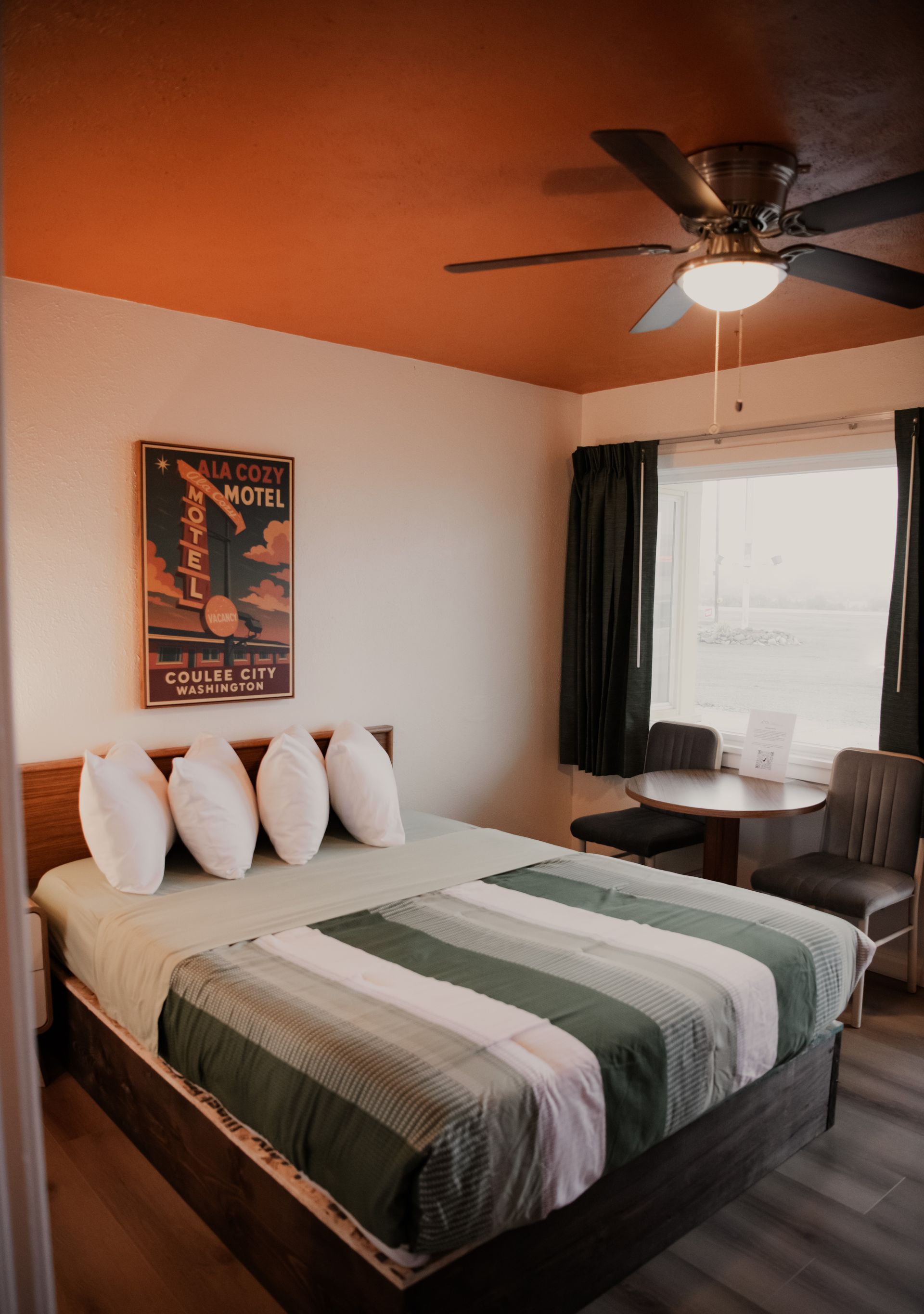 Hotel room with a bed, TV, dresser, microwave, and view of the bathroom. Green and brown bedspread, tan walls.