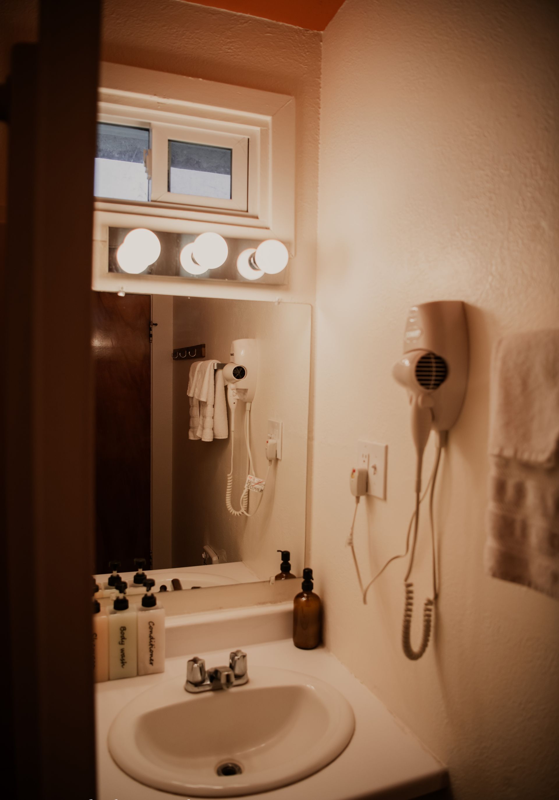 Bathroom with sink, mirror, and light fixture. White walls, hair dryer, and towels.