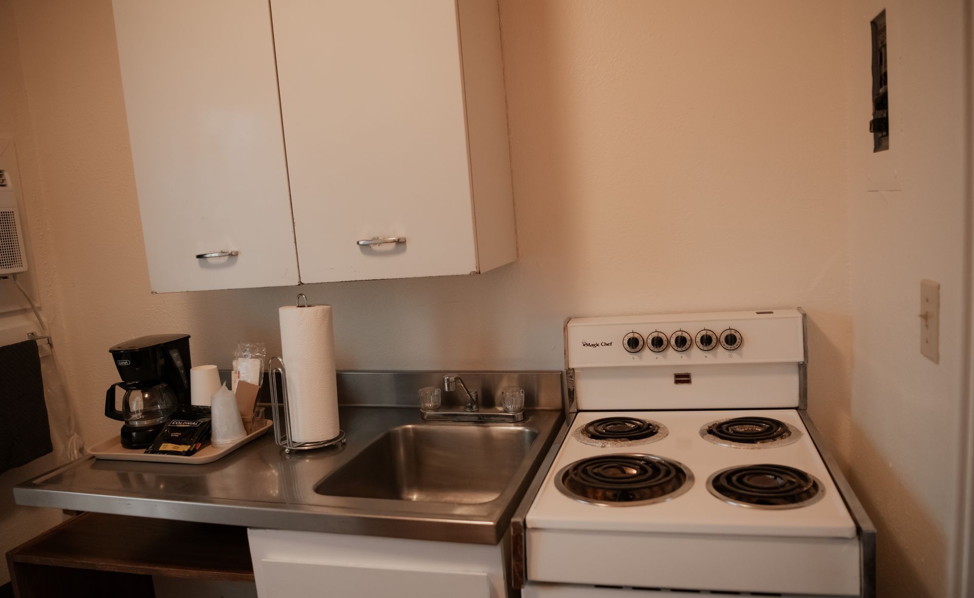 Small kitchen with a stove, sink, countertop, cabinet, and coffee maker.
