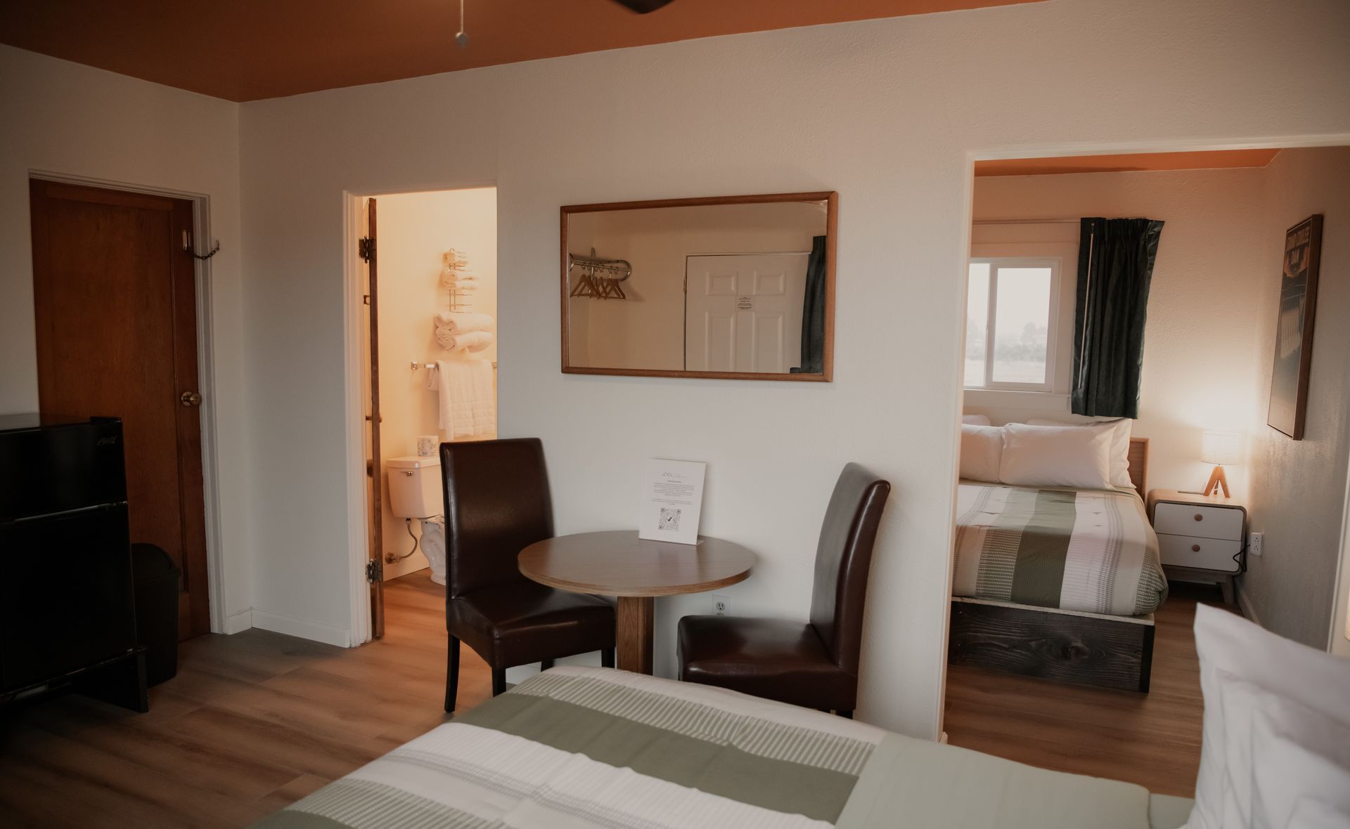 Interior view of a motel room with a dining table, chairs, bed, and a bathroom visible.