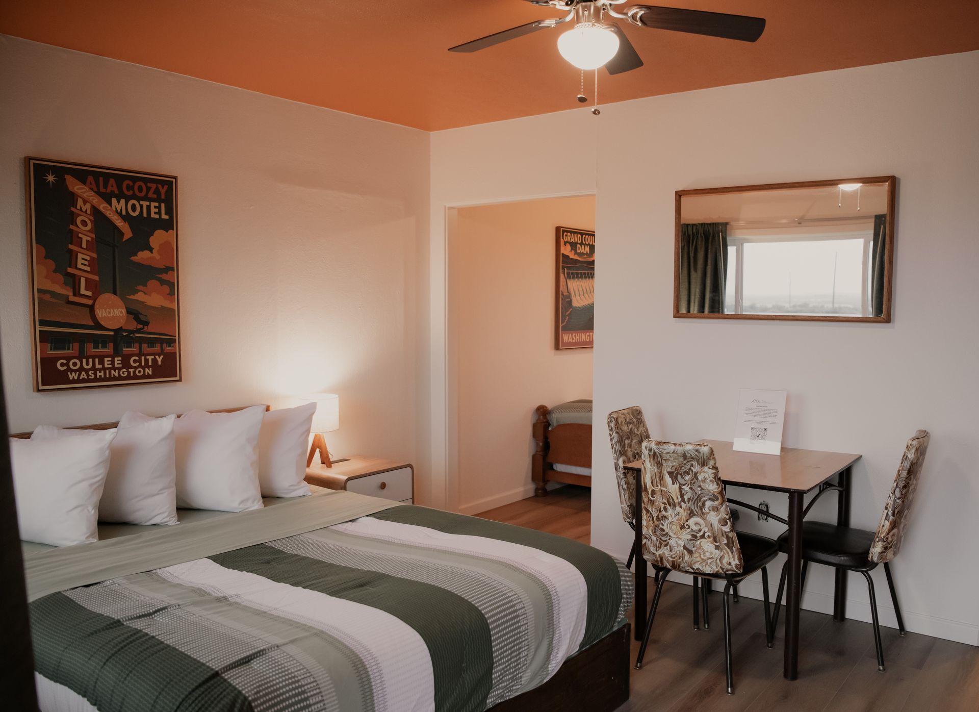 Bedroom interior with a bed, table, chairs, and artwork; orange ceiling.