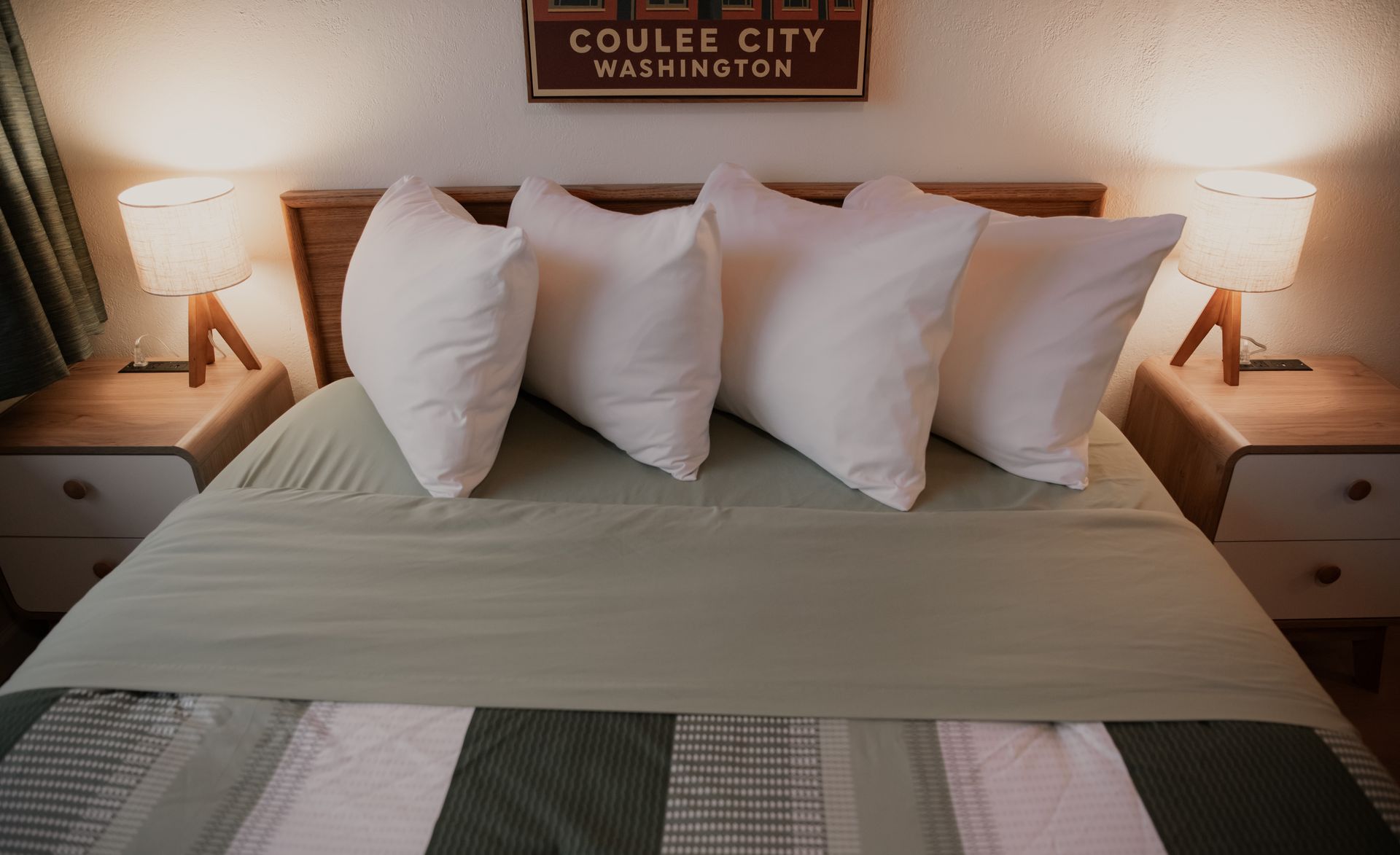 Bedroom with bed, white pillows, bedside tables, lamps, and a sign that says Coulee City, Washington.