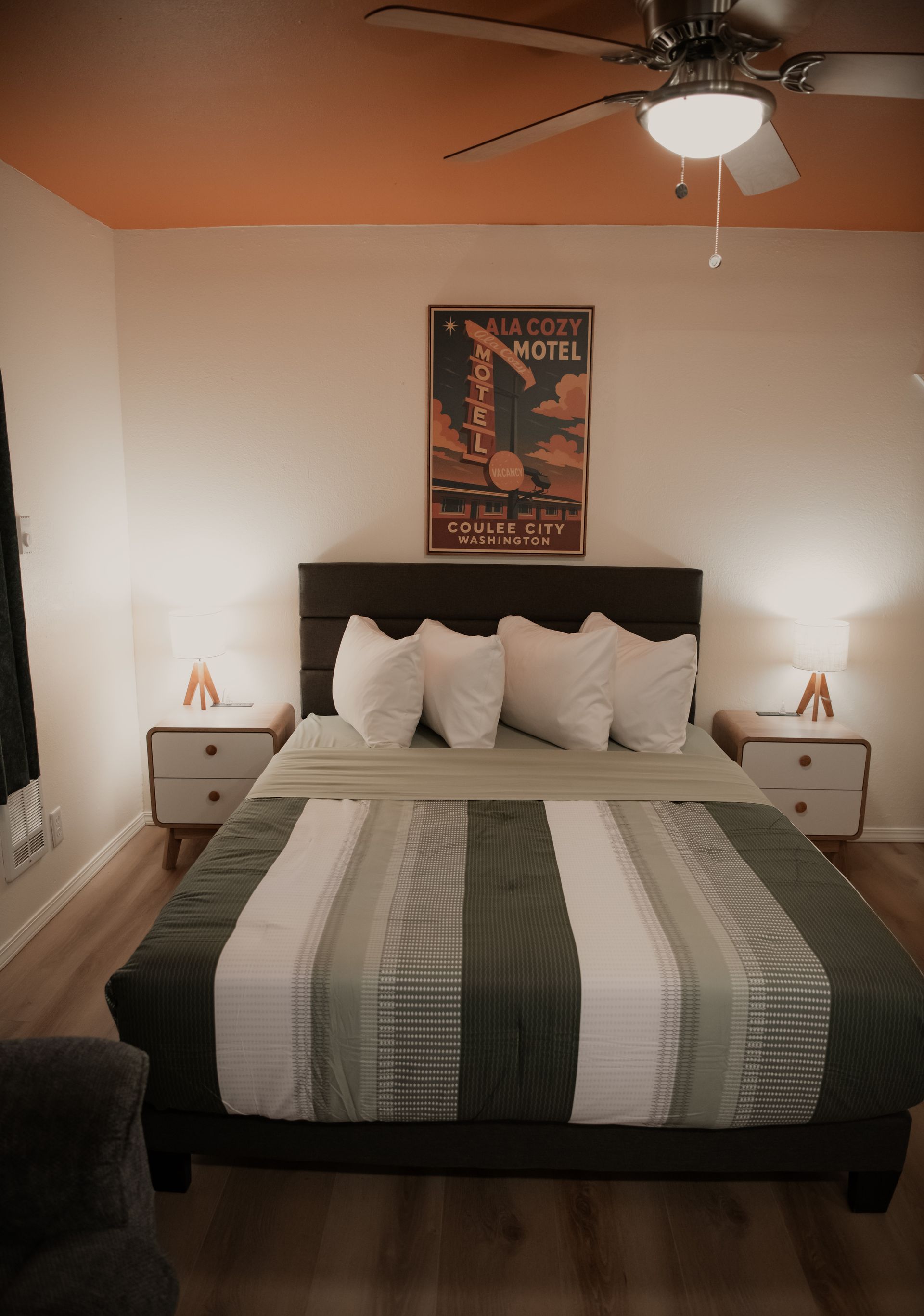 A bed with white pillows, a green and white striped blanket, and a chest of drawers in a room with a window.