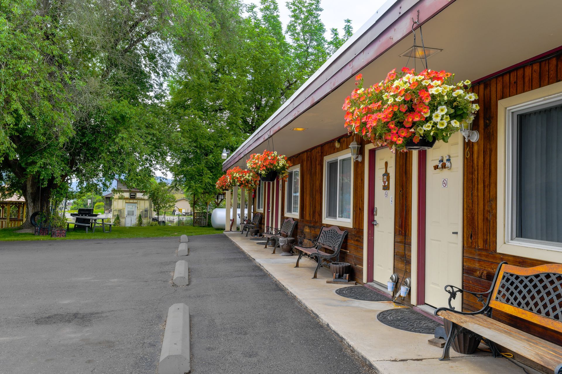 Exterior of a motel with brown wooden siding, doors with hanging flower baskets, benches, and a gravel parking lot.