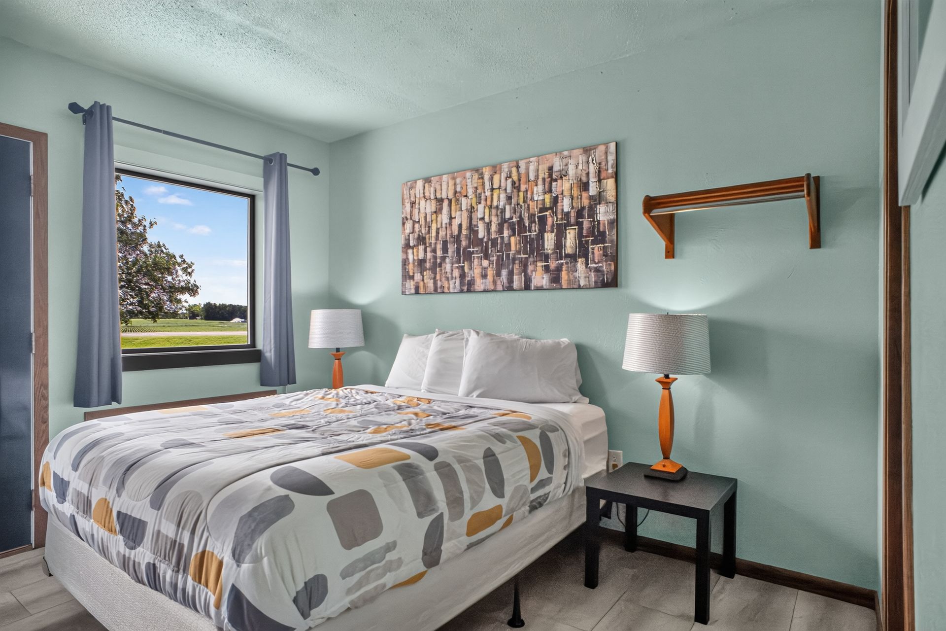 A wooden bed with a white comforter and yellow pillow in a bedroom with a nightstand and shelf.