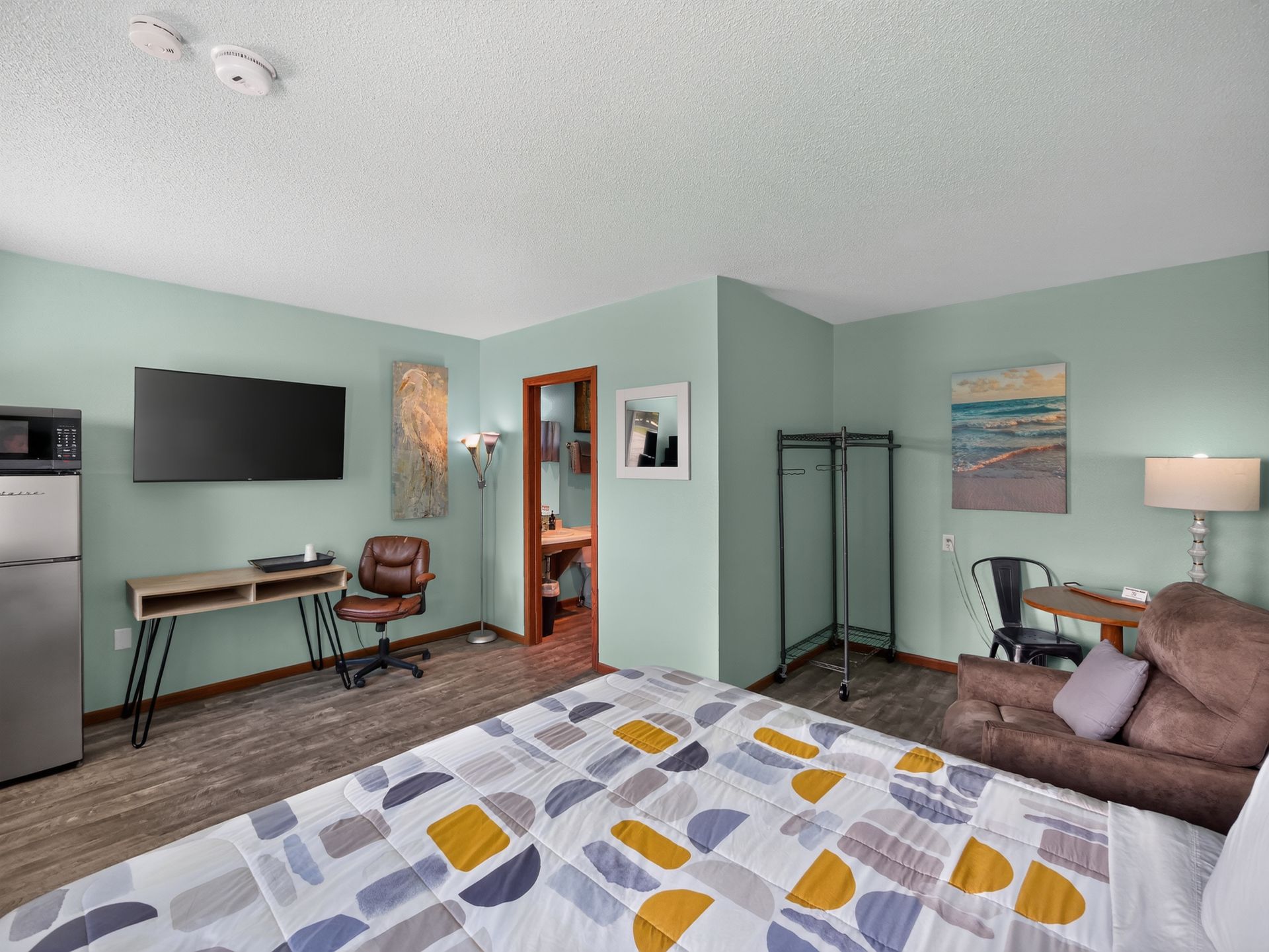 A bedroom with a wooden rocking chair, lamp on a nightstand, and a bed with white linens.