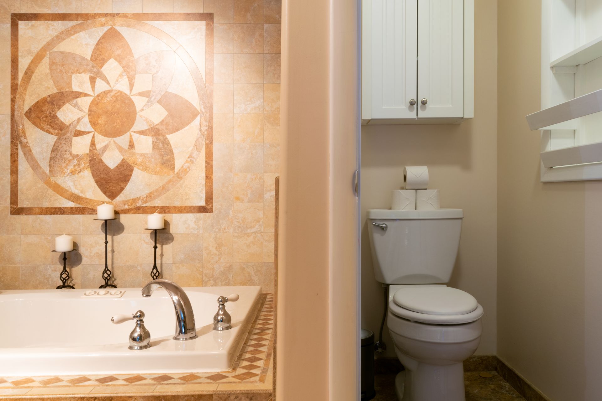 Bathroom interior with a bathtub, toilet, and decorative tilework. Beige walls and a flower mosaic above the tub are visible.