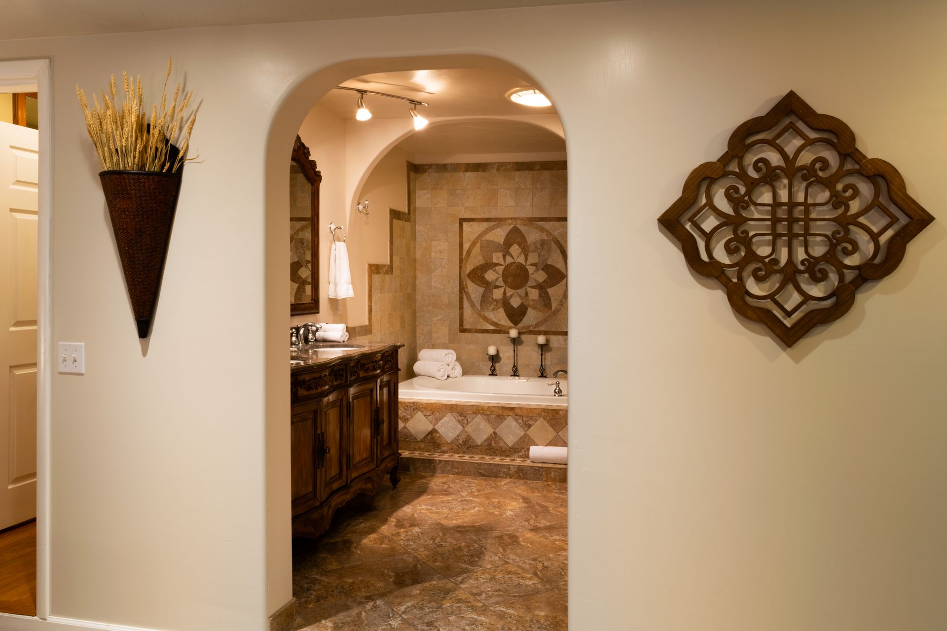 Beige hallway leads to a luxurious bathroom with a wooden vanity, a patterned tile wall, and a bathtub.