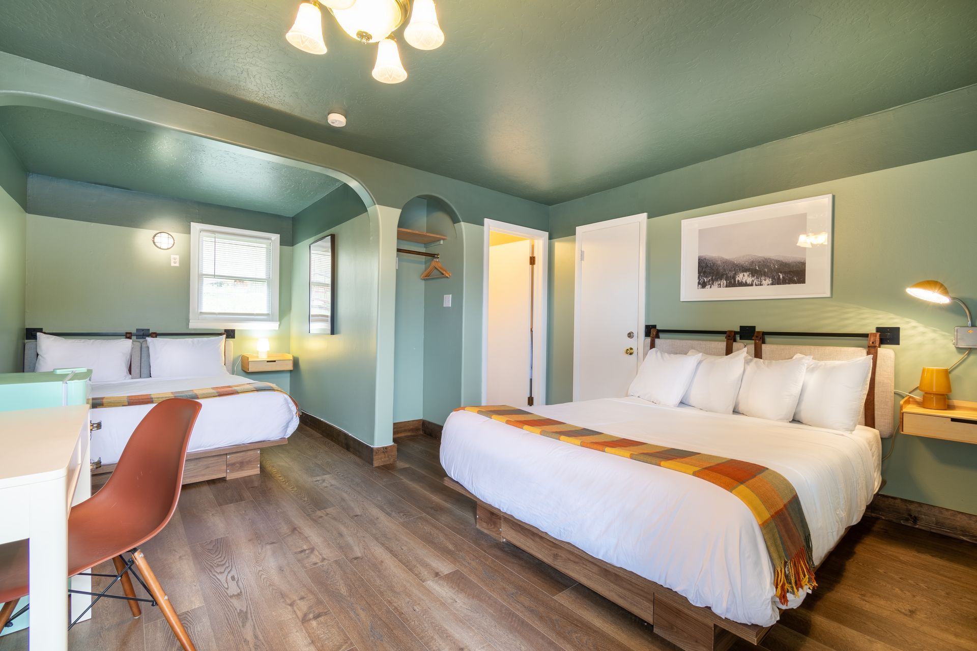 A hotel room with two beds, a desk, and a door. 