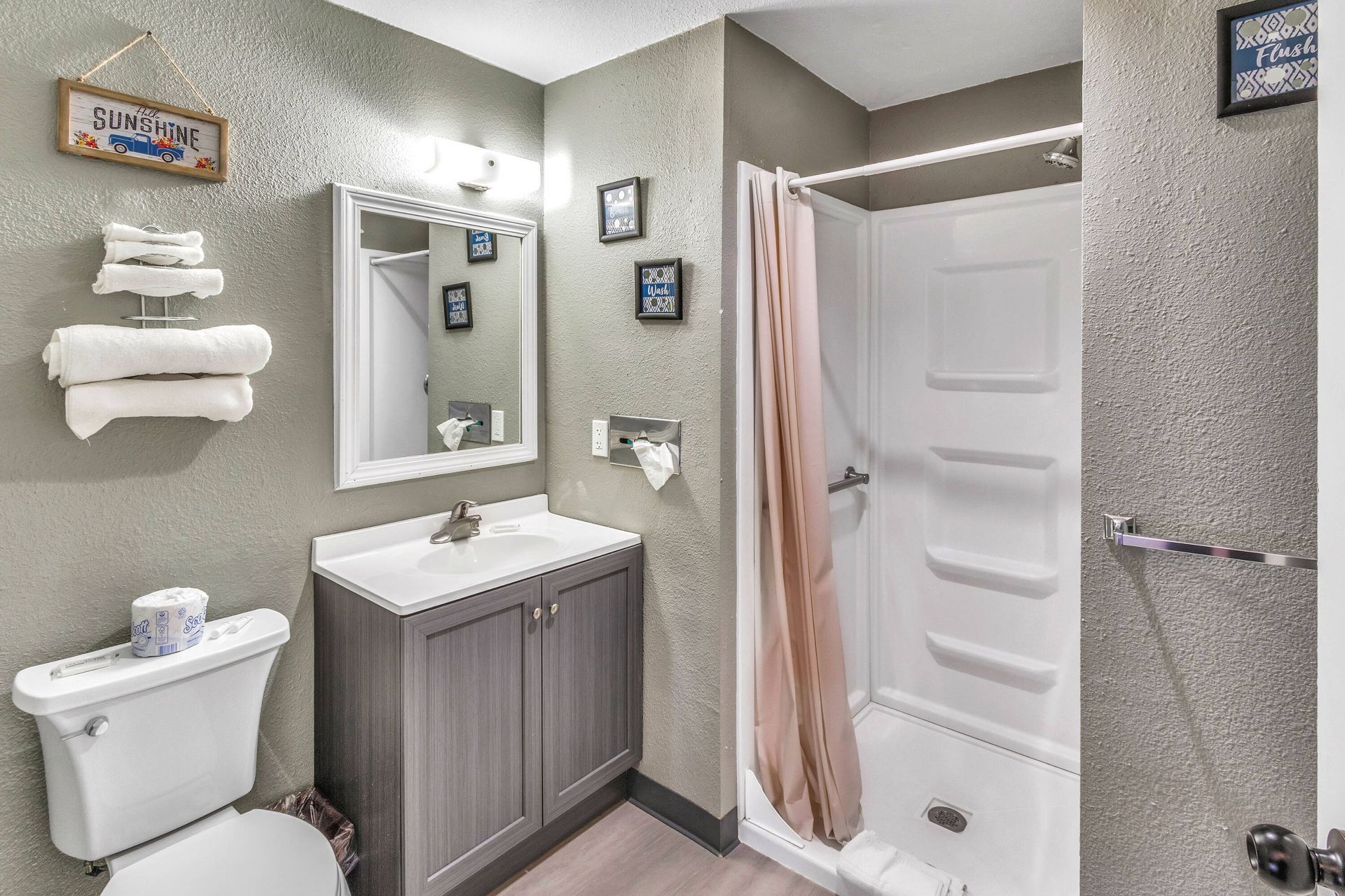 Bathroom with a gray vanity, white toilet, shower with a pink curtain, and towel rack with towels.