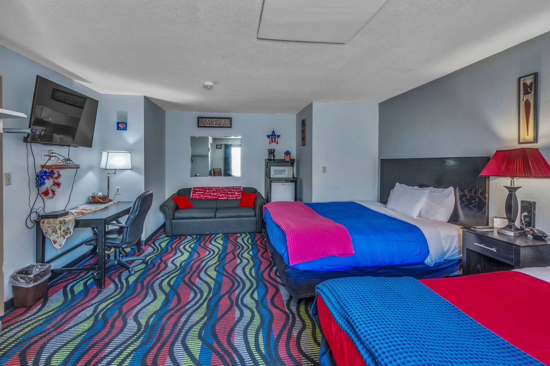 Hotel room with two beds, a couch, desk, and colorful patterned carpet.