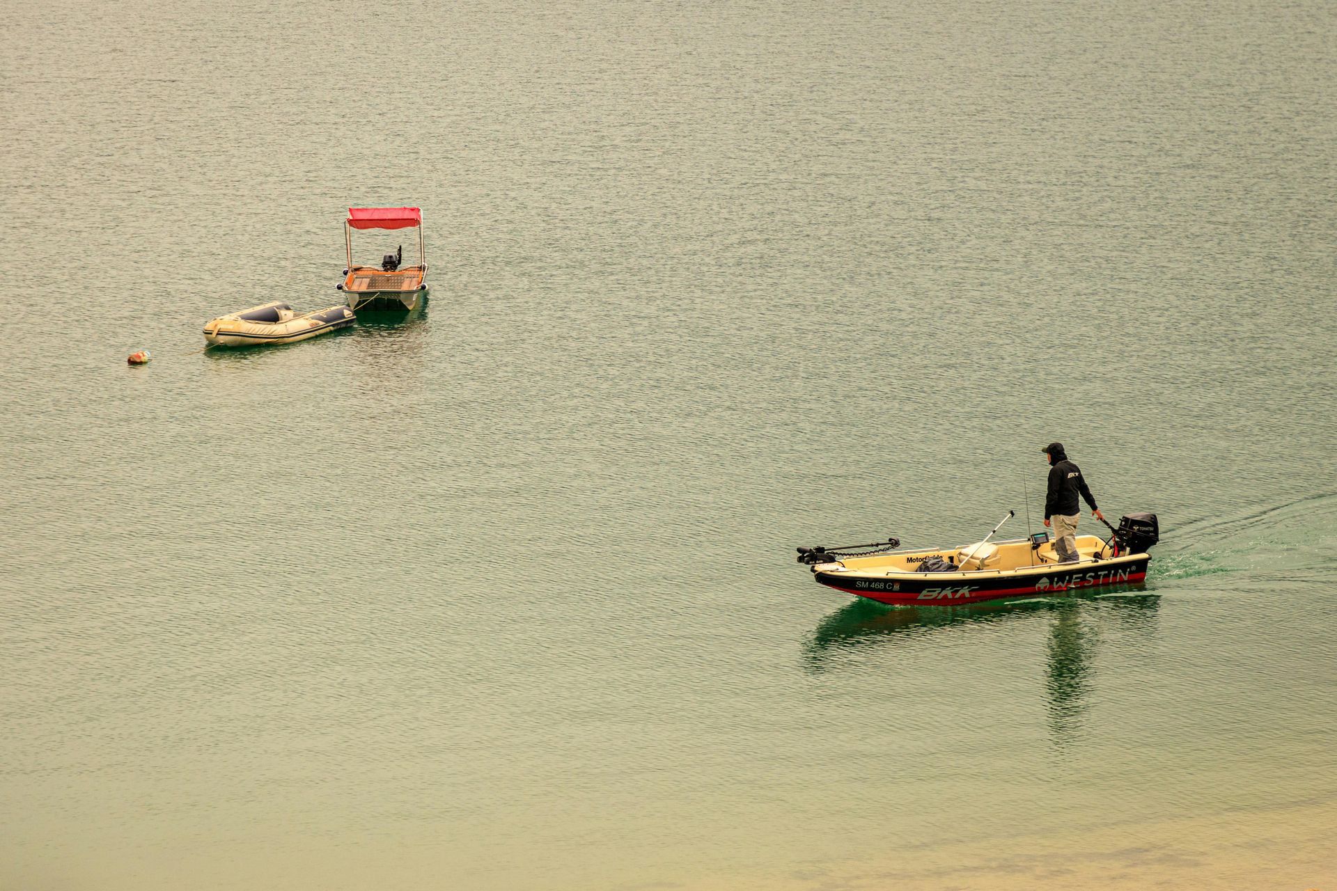 A person operates a small boat on the water near a dock with a red canopy.