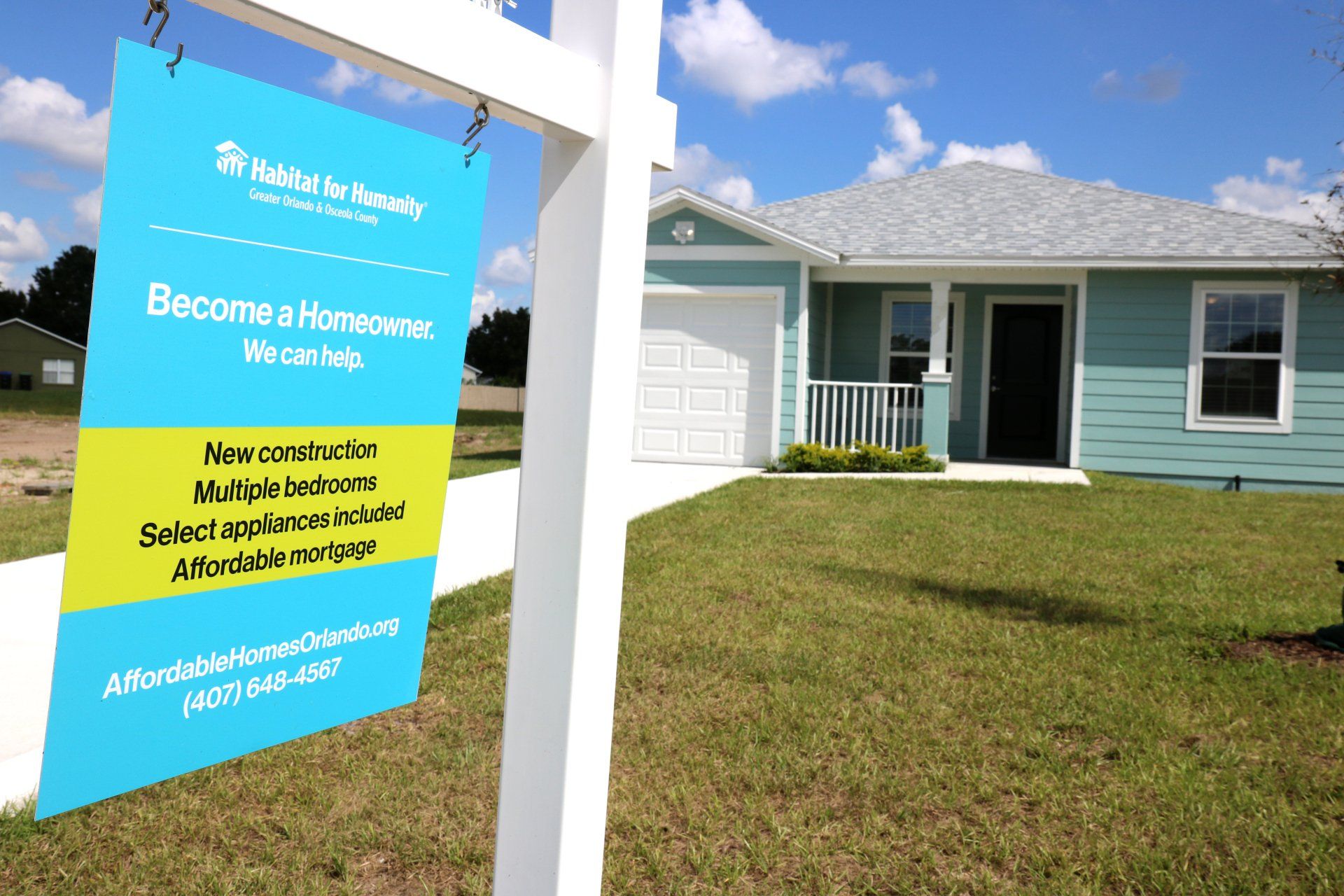 Uma placa de "Vende-se" está em frente a uma casa azul.