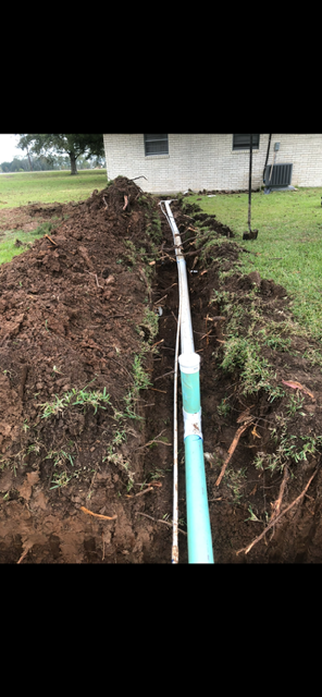 A green pipe is being installed in the dirt in front of a house.