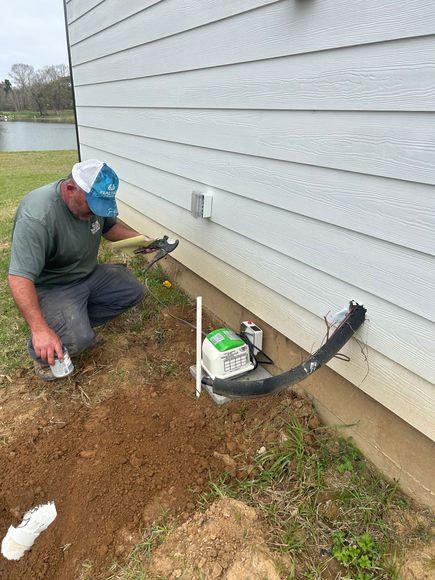 A man is kneeling in the dirt next to a house.