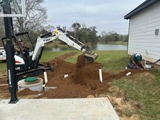 A man is digging a hole in the ground in front of a house.