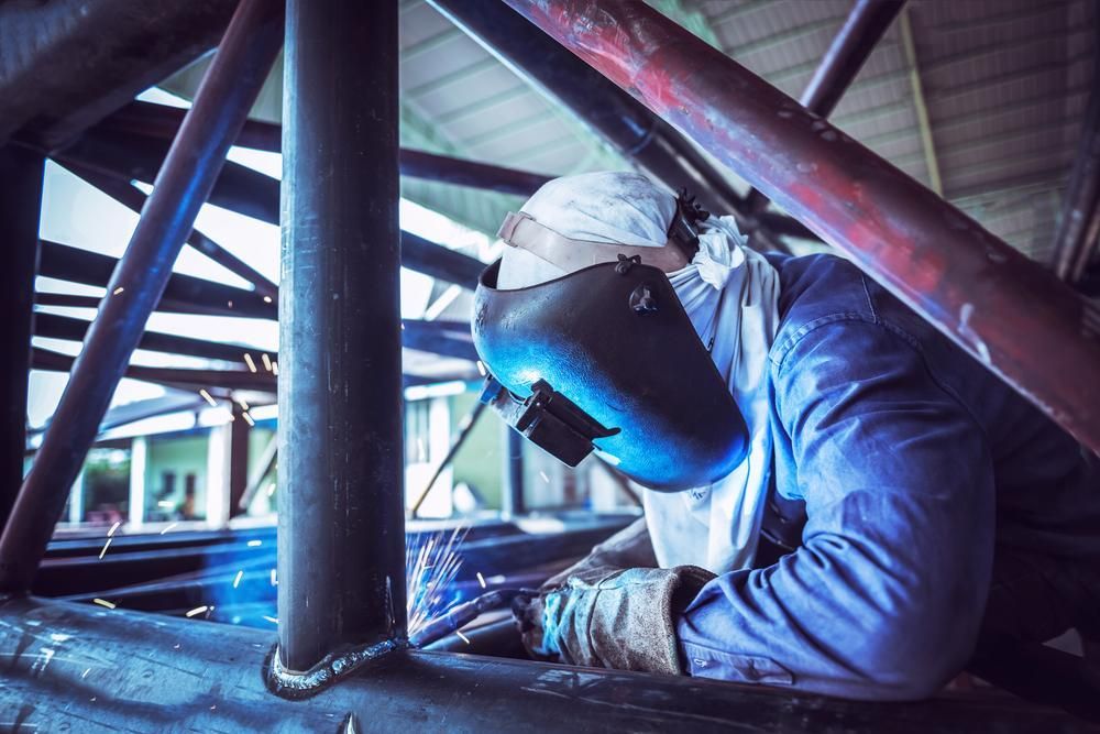 A Man Wearing a Welding Mask is Welding a Pipe in a Factory — Kymar Steel Fabrications in Central Coast, NSW