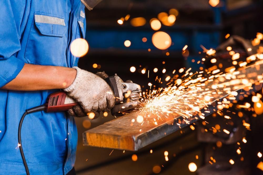 A Man is Grinding a Piece of Metal in a Factory — Kymar Steel Fabrications in Newcastle, NSW