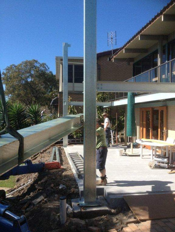 A Man is Standing Next to a Metal Pole in Front of a House — Kymar Steel Fabrications in Teralba, NSW