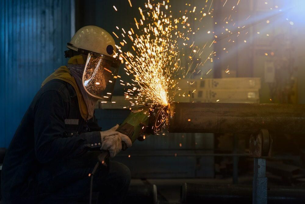 A Man is Grinding a Piece of Metal With a Grinder in a Factory — Kymar Steel Fabrications in Newcastle, NSW