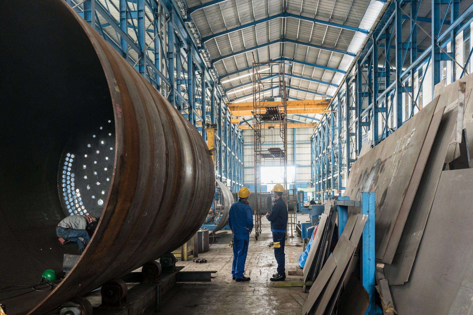 Two Men Are Standing in a Factory Looking at a Large Pipe — Kymar Steel Fabrications in Teralba, NSW