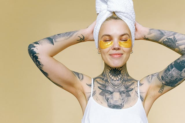 A Woman with Tattoos Has a Towel Wrapped Around Her Head and Eye Patches on Her Face — Rejuved in Bateau Bay, NSW