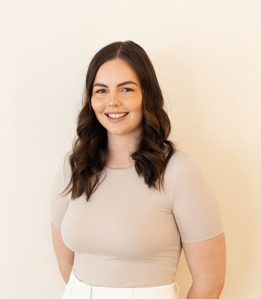 A Woman in A Tan Shirt and White Pants Is Standing in Front of A White Wall — Rejuved in Bateau Bay, NSW