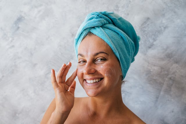 A Woman with A Towel Wrapped Around Her Head Is Smiling and Touching Her Face — Rejuved in Bateau Bay, NSW